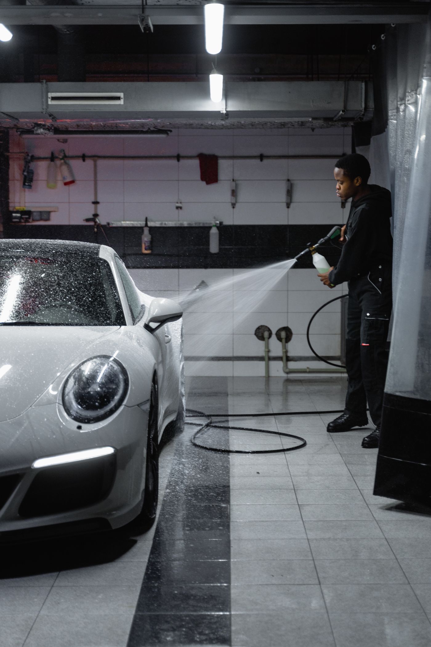 A DnA detailer spraying down the front end of a white Porsche during an exterior detail