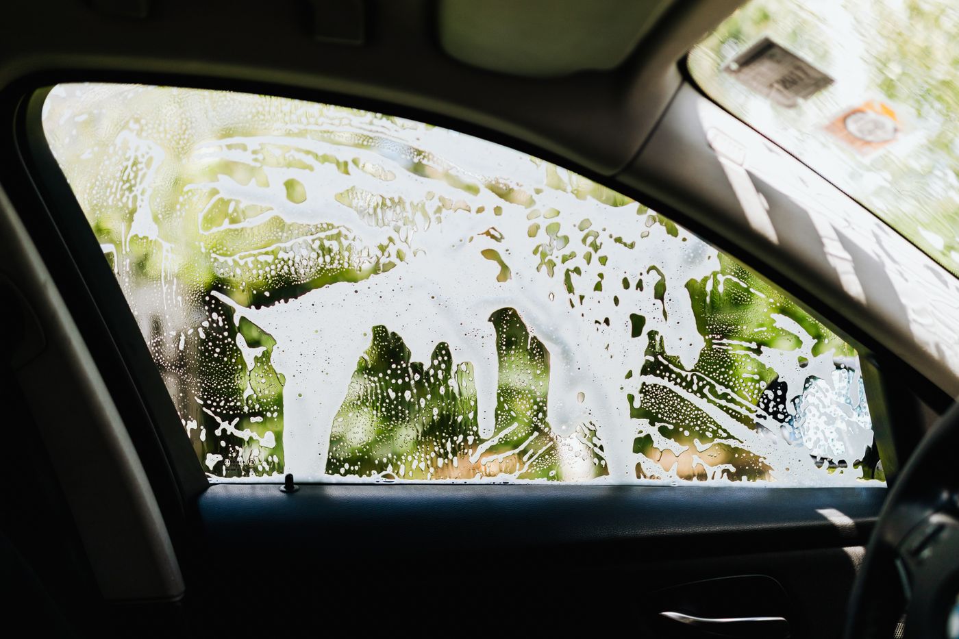 Cleaning foam being rinsed across a car side window, seen from inside the cabin