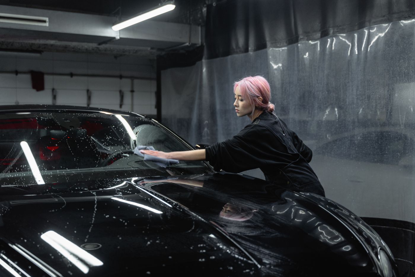 A DnA detailer hand-wiping the panel of a black luxury car in soft garage light